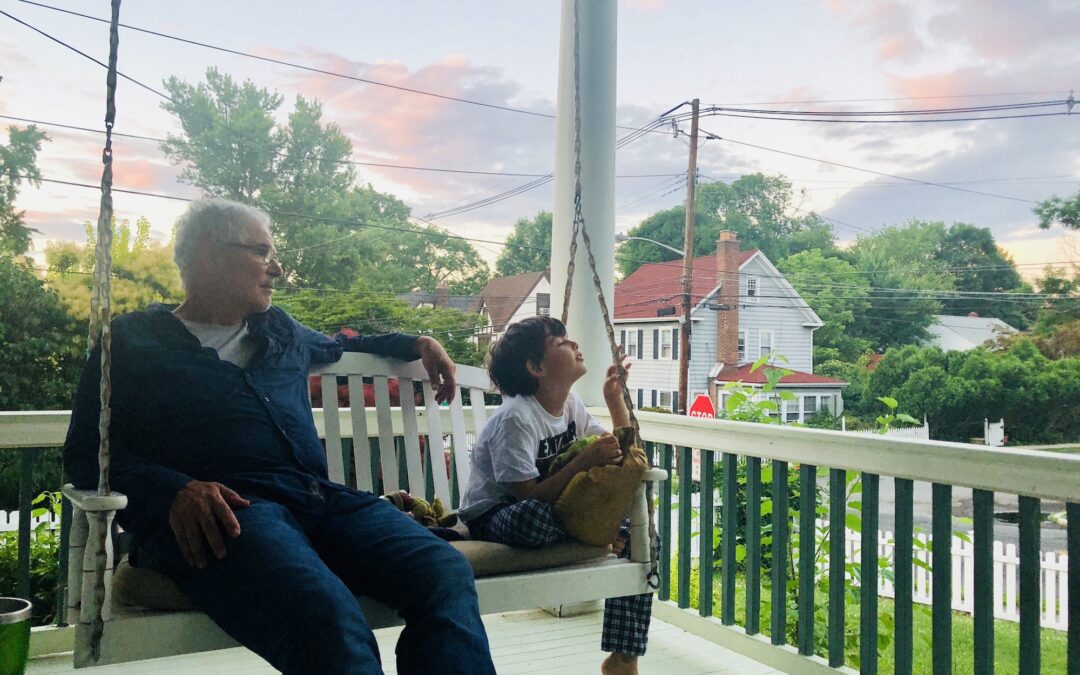 Grandfather and grandson on white porch swing with city in background