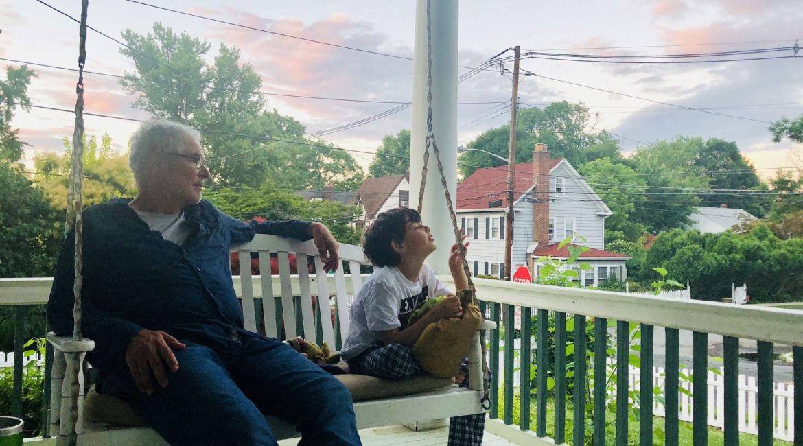 Grandfather and grandson on white porch swing with city in background