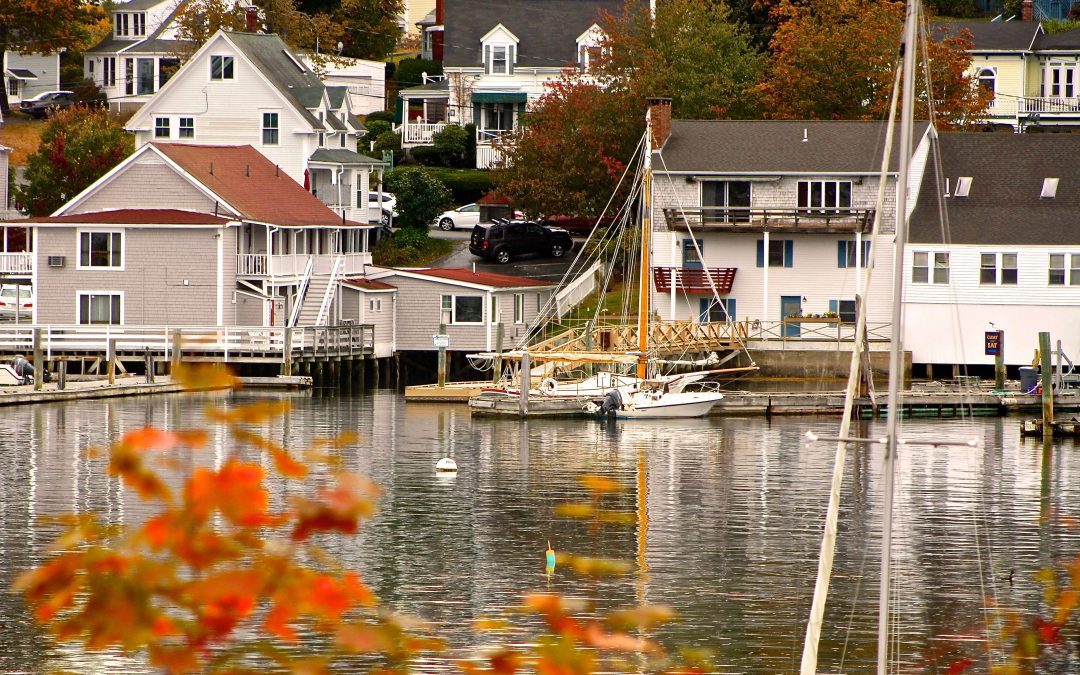 A scenic waterfront village/ White and beige homes are nestled on a hill with water in front. A white boat sits in the harbor.