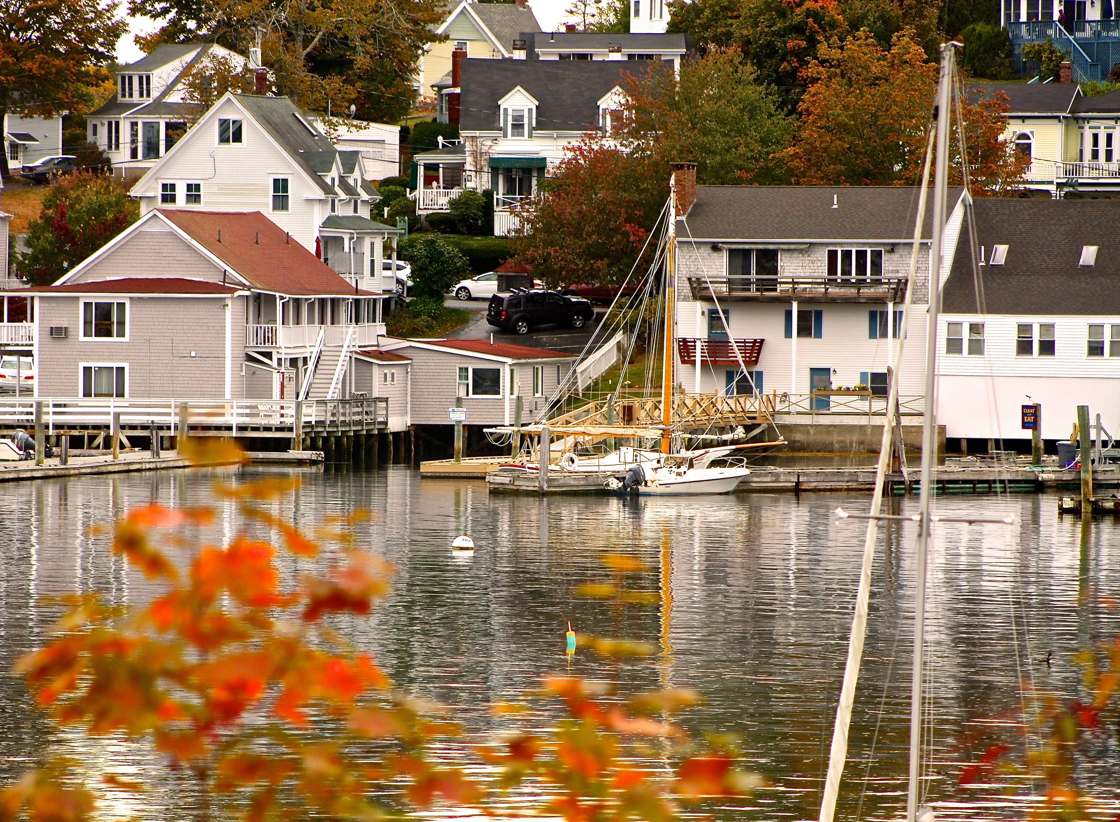 A scenic waterfront village/ White and beige homes are nestled on a hill with water in front. A white boat sits in the harbor.