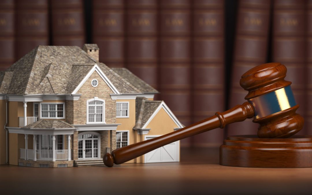 A miniature house sits next to a gavel and law books